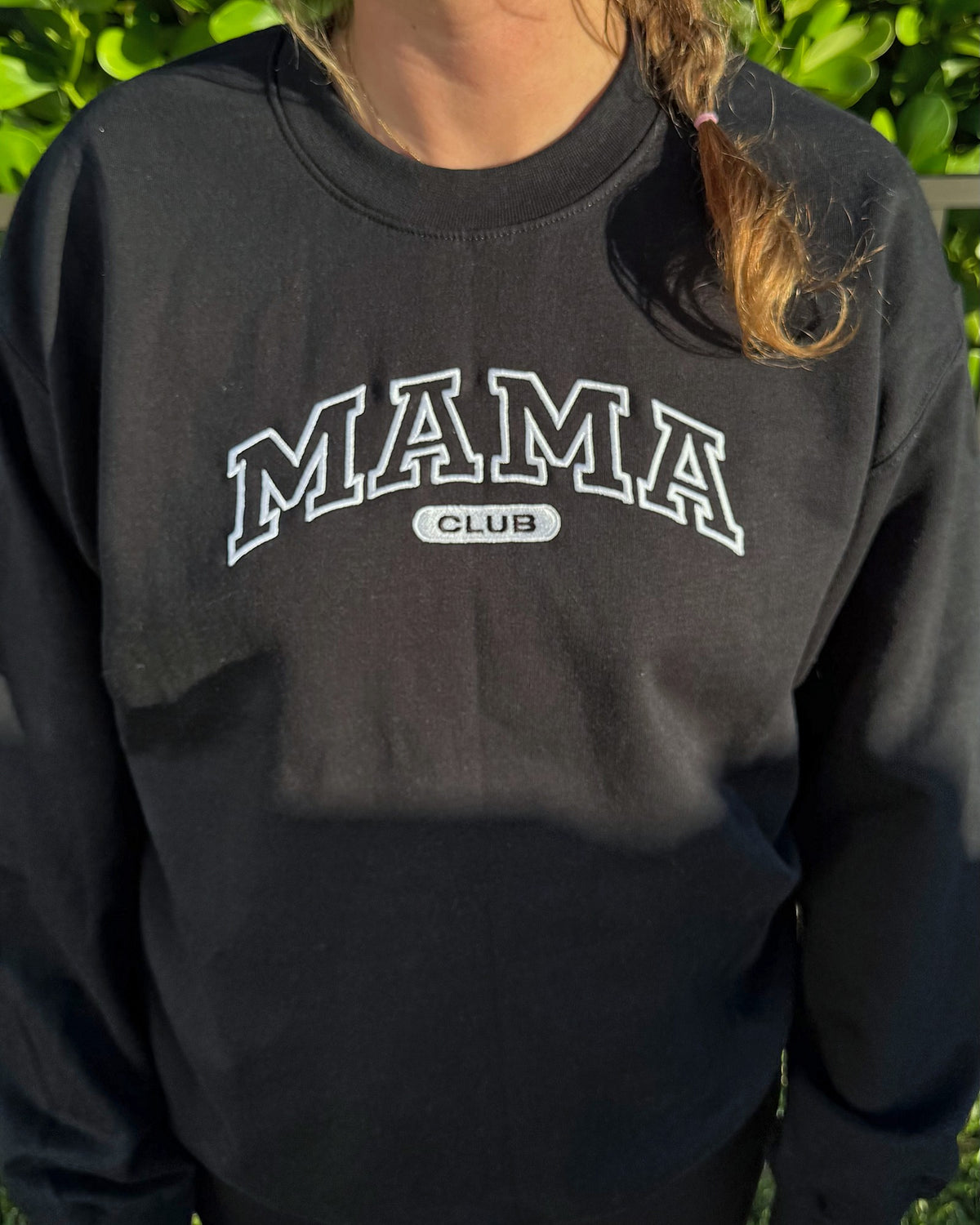 Close-up of the white outline MAMA CLUB embroidery on the black crewneck