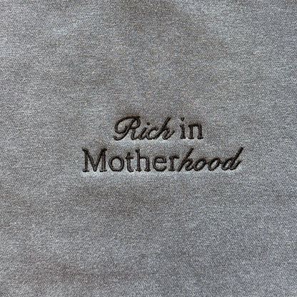 Close-up of the black Rich in Motherhood embroidery on the pepper grey crewneck