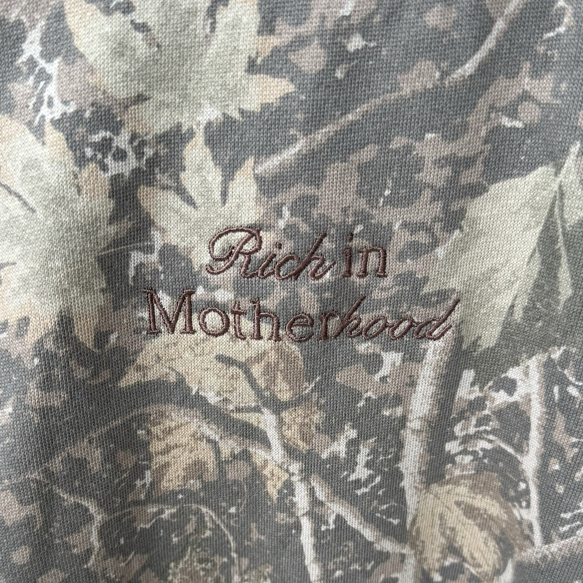 Close-up of the brown Rich in Motherhood script embroidery on Deadwood Camo