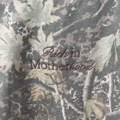 Close-up of the brown Rich in Motherhood script embroidery on Deadwood Camo
