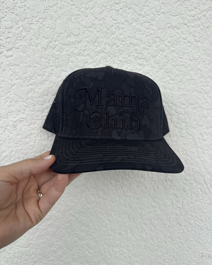 Mama Club black camo trucker, black puff embroidery, held against a white wall
